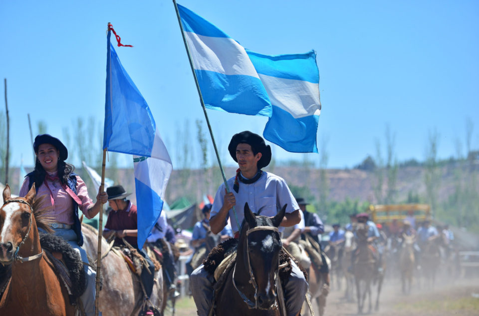 Gauchos cabalgando con bandera argentina