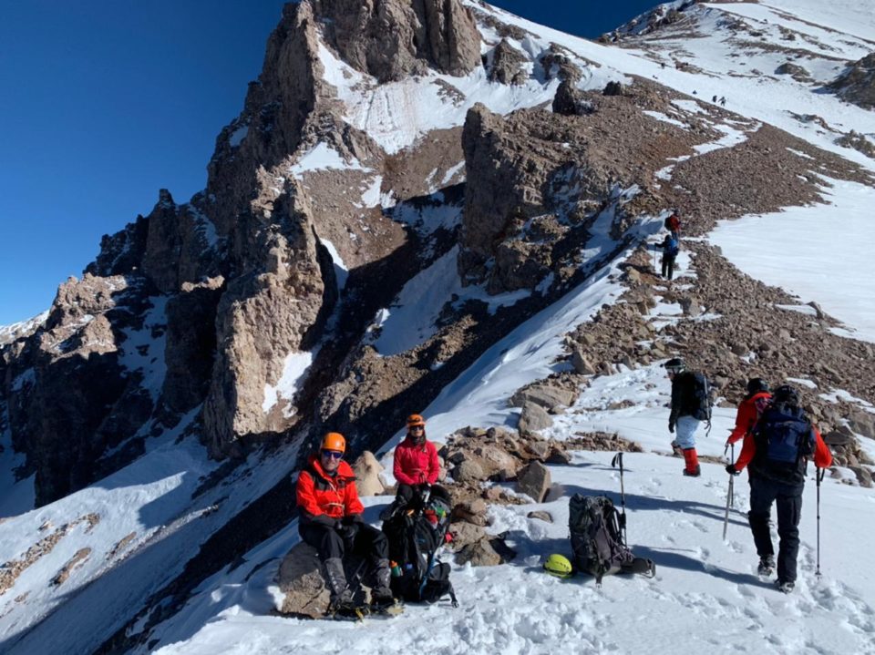 Varios andinistas subiendo por una ladera de roca y nieve y otros sentados descansando