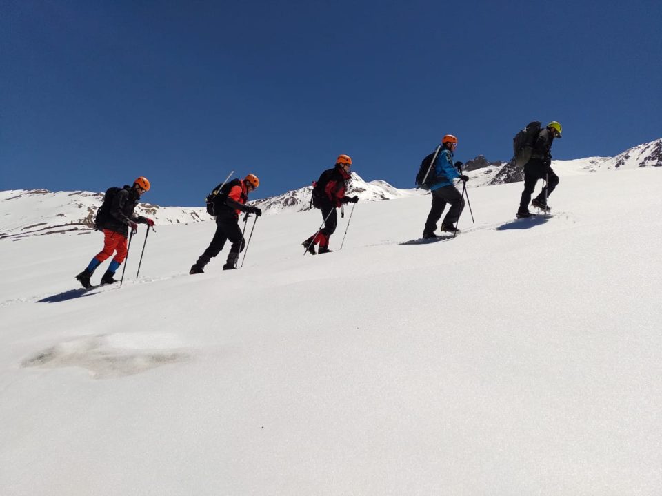 Cinco andinistas subiendo la montaña con nieve con casco, crampones y bastones 